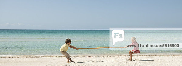 Kinder beim Tauziehen mit Bambus am Strand