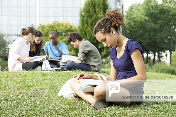 Young woman reading book on grass  group of young people in background