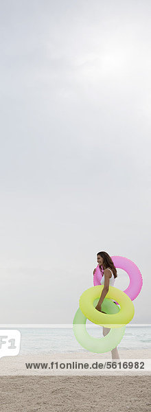 Frau steht am Strand  hält aufblasbare Ringe  Seitenansicht