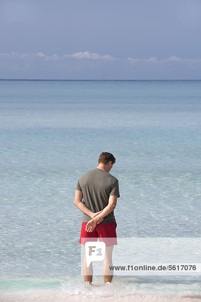 Mann steht knöcheltief im Wasser und betrachtet den Ozean  Rückansicht
