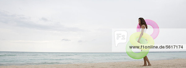 Frau steht am Strand  hält aufblasbare Ringe  Seitenansicht