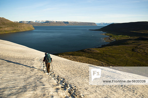 Wanderin durchquert das Schneefeld  Blick auf Ort Hesteyri  Fjord Hesteyrarfjör_ur  Hesteyrarfjördur  Hornstrandir  Westfjorde  Island  Europa