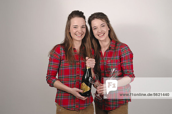 Twin sisters holding a bottle of sparkling wine and champagne glasses