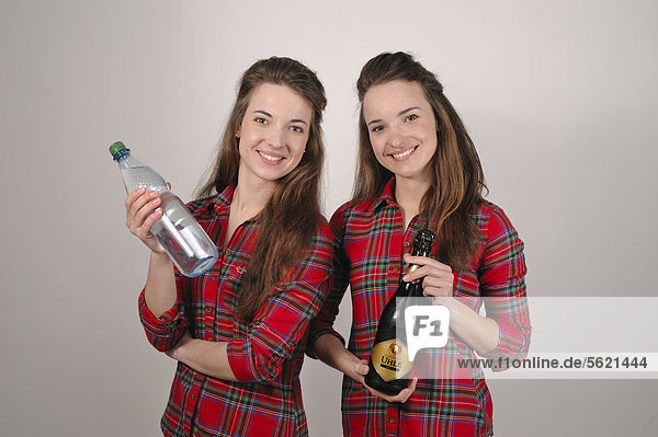 Zwillingsschwestern  eine mit einer Flasche Mineralwasser  einer mit einer Flasche Sekt
