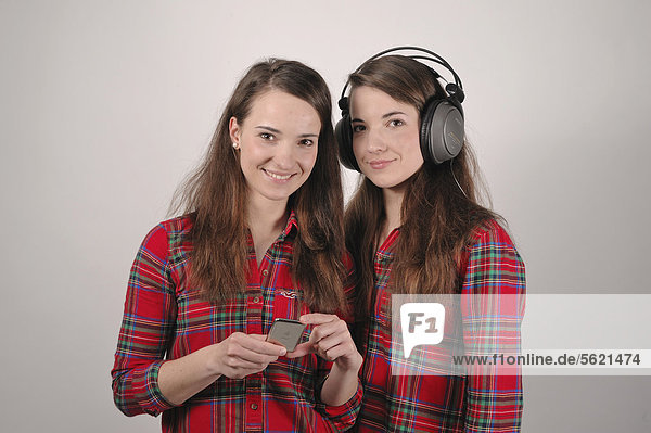 Twin sisters  one holding an iPod  the other listening to headphones