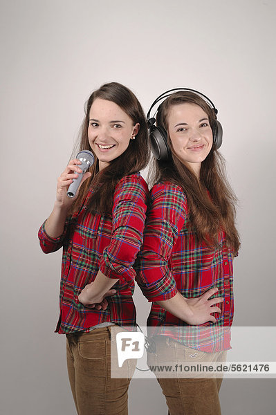 Twin sisters  one singing into a microphone  while the other listens with headphones