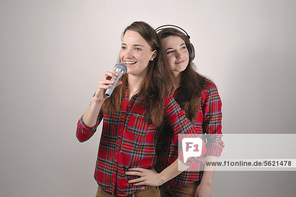 Twin sisters  one singing into a microphone  while the other listens with headphones