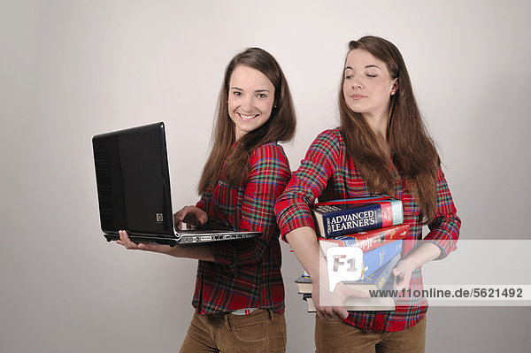 Twin sisters  one holding a laptop  the other holding a stack of books