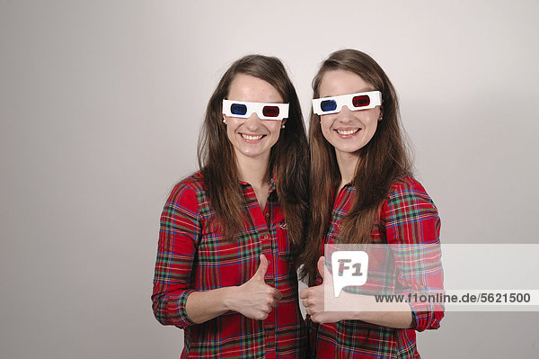 Twin sisters wearing 3D glasses holding up their thumbs