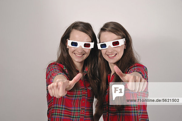 Zwillingsschwestern mit 3D-Brillen halten Daumen hoch