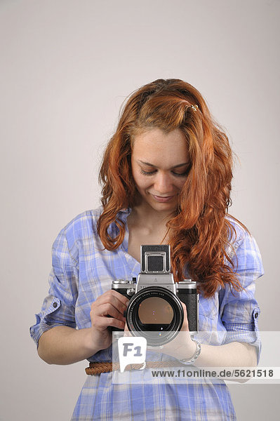 Young woman with red hair taking a photograph with an analog medium format camera Pentacon Six