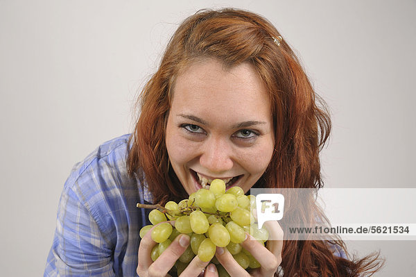 Junge Frau mit roten Haaren isst grüne Weintrauben