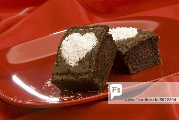 Brownies mit Puderzuckerherzen auf rotem Teller