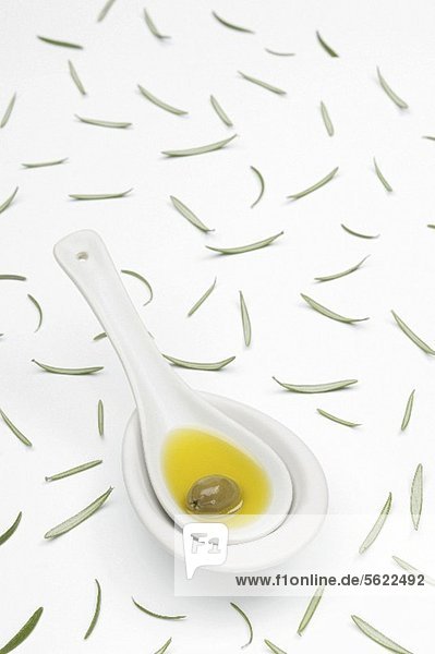 Löffel mit Olivenöl und Olive und verstreute Rosmarinblätter