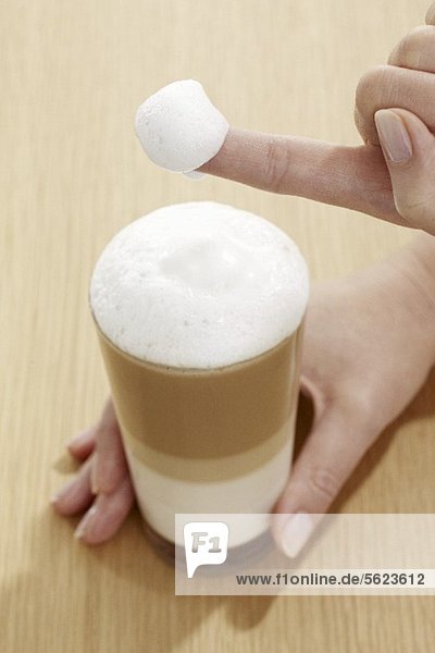 Finger mit Milchschaum von einem Glas Latte Macchiato