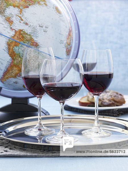 Three glasses red wine on a silver platter in front of a globe