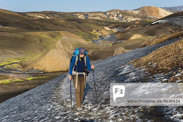 Wanderin durchquert Schneefeld  mit Schnee und Asche bedeckte Rhyolith-Berge am Wanderweg Laugavegur  Landmannalaugar-Hrafntinnusker  Fjallabak Naturschutzgebiet  Hochland  Island  Europa