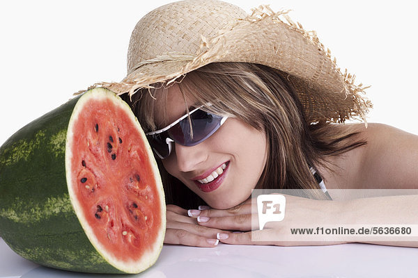 Junge Frau mit Sonnenbrille und Sonnenhut vor Wassermelone
