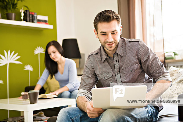 Young man at home  with a laptop  young woman at back