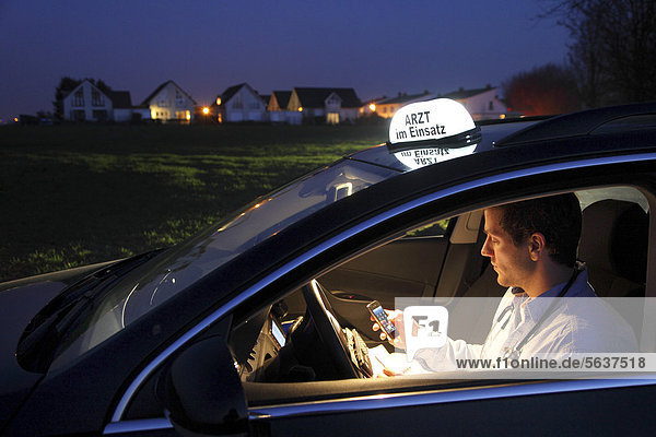 'Young GP  general practitioner working in the country  making phone call and taking notes in his car after an evening home visit  car displaying the sign ''Arzt im Einsatz''  German for ''doctor on call''  Ickten  North Rhine-Westphalia  Germany  Europe'