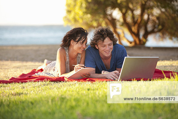 Couple using laptop on picnic blanket