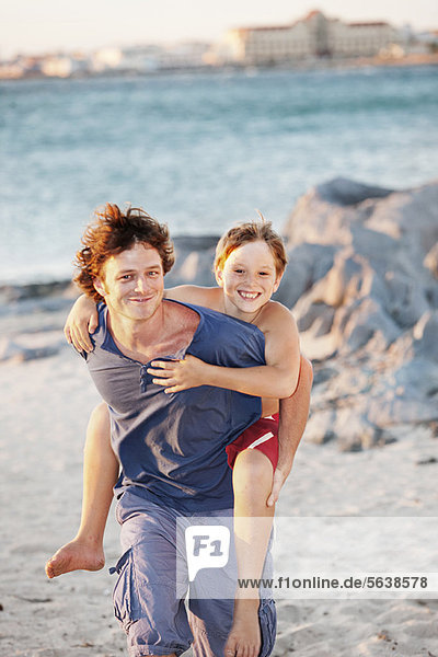 Father carrying son piggyback on beach