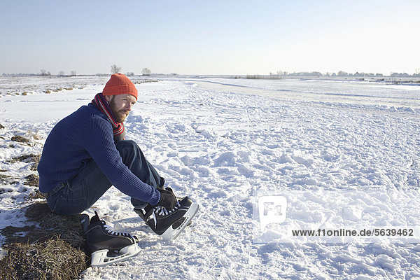 Man lacing up ice skates in snowy field
