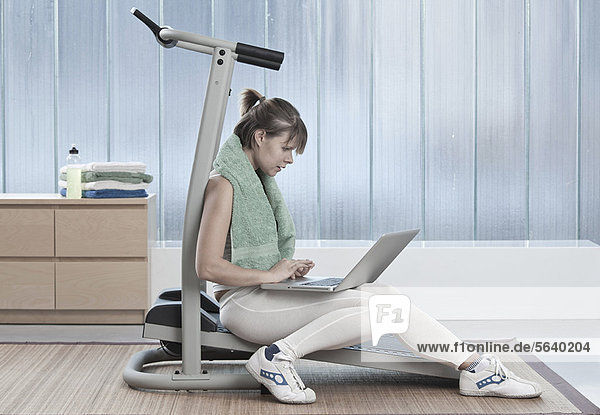 Woman using laptop on exercise machine