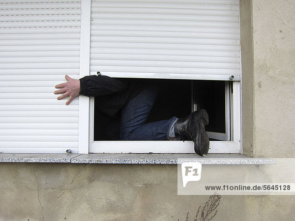 Ein Mann  der durch ein Fenster klettert.