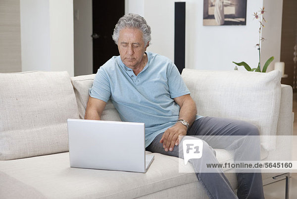 A senior man sitting on a couch using a laptop
