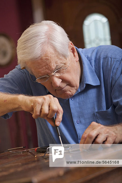 Ein älterer Mann  der eine Brille repariert.