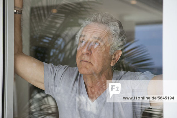 Ein älterer Mann  der aus dem Fenster schaut.