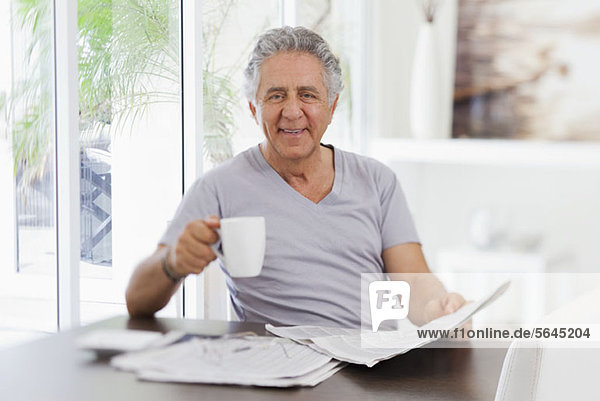 Ein fröhlicher älterer Mann  der die Zeitung liest und Kaffee trinkt.
