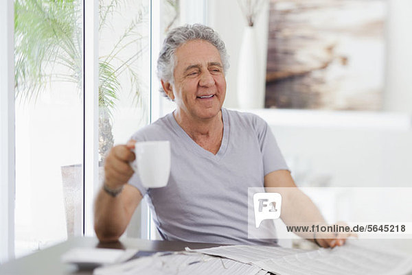 Ein fröhlicher Senior mit einer Tasse Kaffee und einer Zeitung.