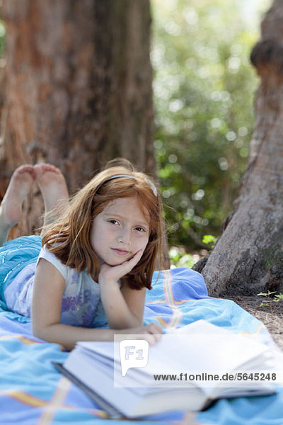 Mädchen auf Decke liegend im Park mit Buch
