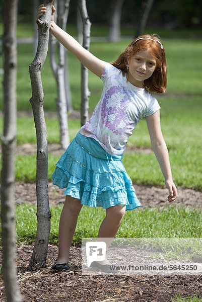 Junges Mädchen im Park hält sich am Baum fest