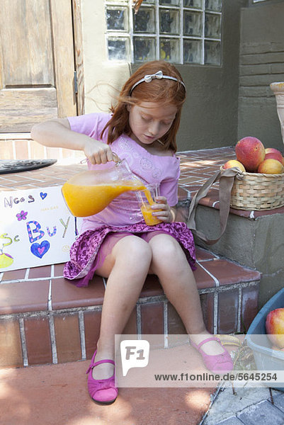 Mädchen verkauft Äpfel auf der Veranda und gießt Saft aus der Kanne.