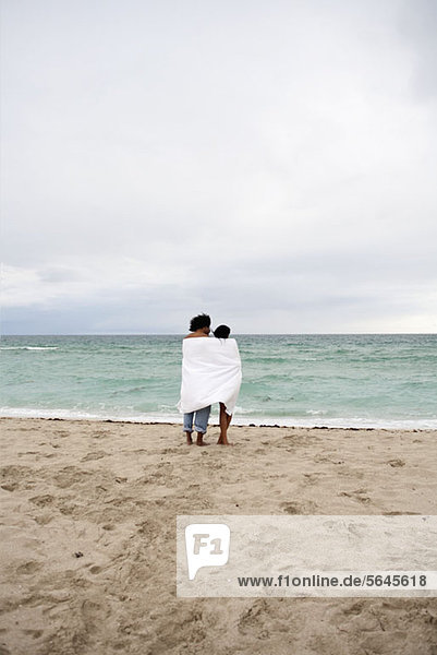 Ein junges Paar in ein Strandtuch gewickelt  das am Strand steht.