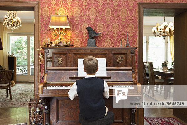 Ein Junge  der auf einem altmodischen Klavier übt.