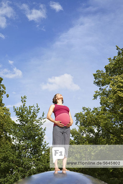 Eine schwangere Frau  die in der Natur steht und sich in der Sonne sonnt.