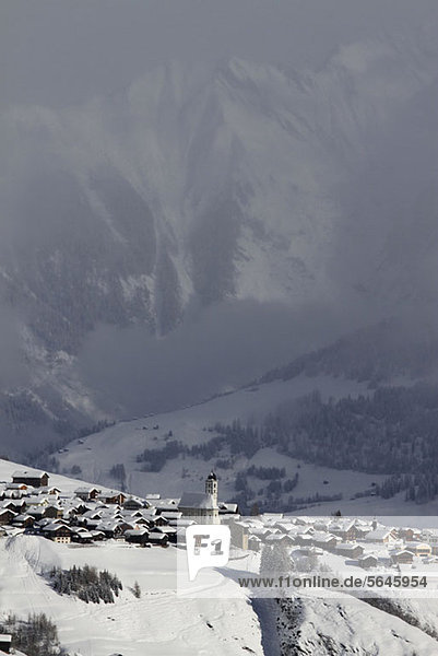 Verschneites Dorf mit Bergkette und Tal im Hintergrund
