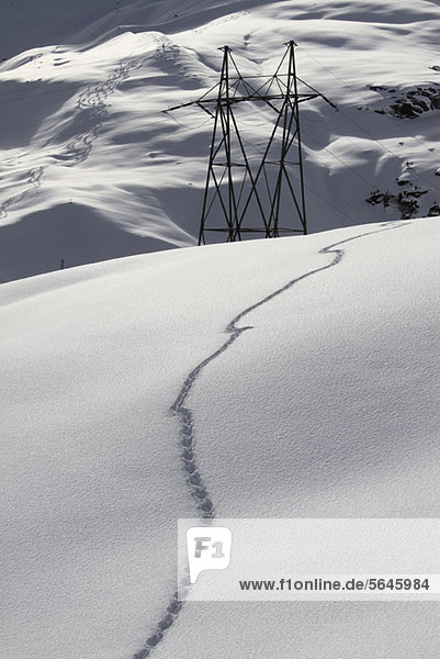 Schneefußabdrücke auf dem Hügel mit elektrischem Pylon im Hintergrund
