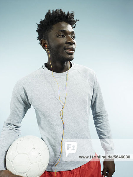 Ein junger Mann trägt Ohrstöpsel und hält einen Fußball.
