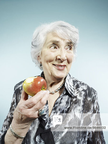 Eine ältere Frau hält einen Apfel mit einem Biss davon.