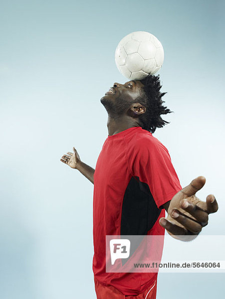Ein junger Mann  der einen Fußball auf der Stirn balanciert.