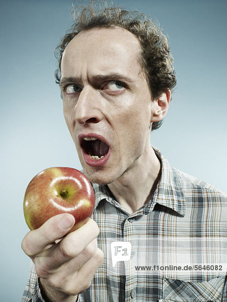 Ein Mann mit Stirnrunzeln  der sich darauf vorbereitet  in einen Apfel zu beißen.