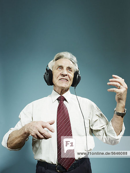 Ein älterer Mann  der Kopfhörer trägt und Luftgitarre spielt.