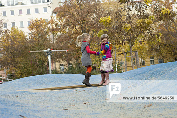 Zwei Mädchen springen auf einem kleinen Trampolin im Park.