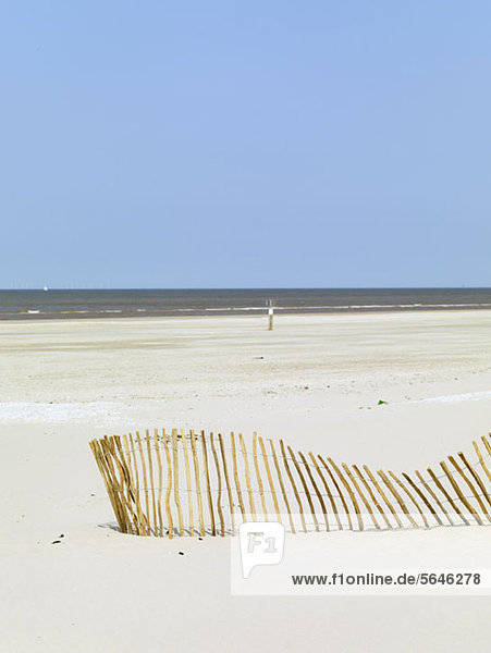 Ein schräger Zaun am Strand und das Meer im Hintergrund