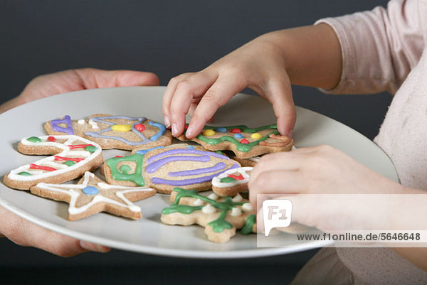 Eine Mutter  die mit ihrer Tochter einen Teller Weihnachtsplätzchen teilt  konzentriert sich auf die Hände.